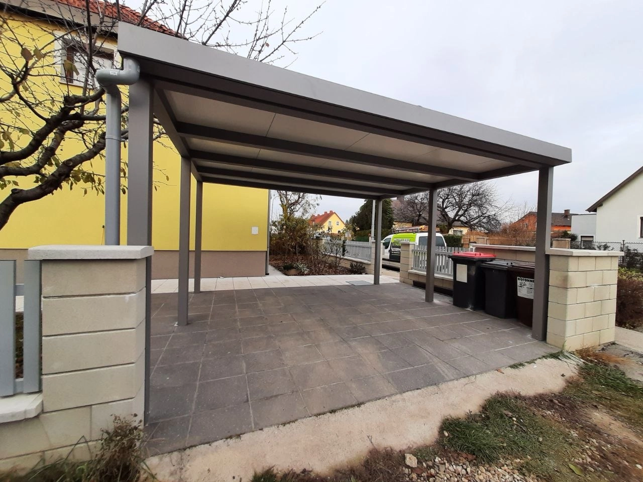 Aluminium-Carport mit geneigtem Dach neben einem gelben Wohnhaus