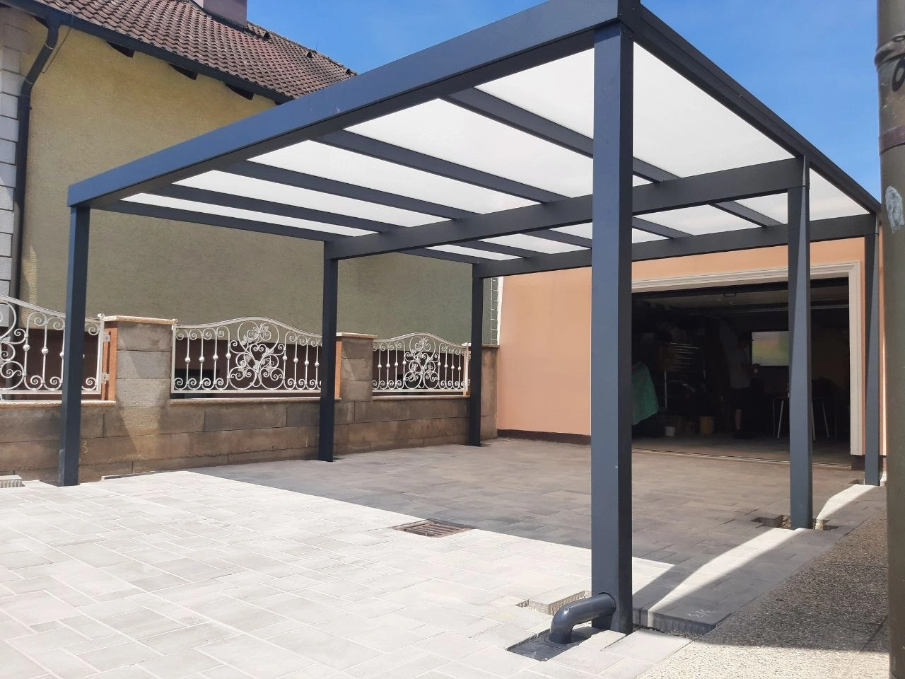Offener anthrazitfarbener Aluminium-Carport mit heller Dacheindeckung vor einer Garage