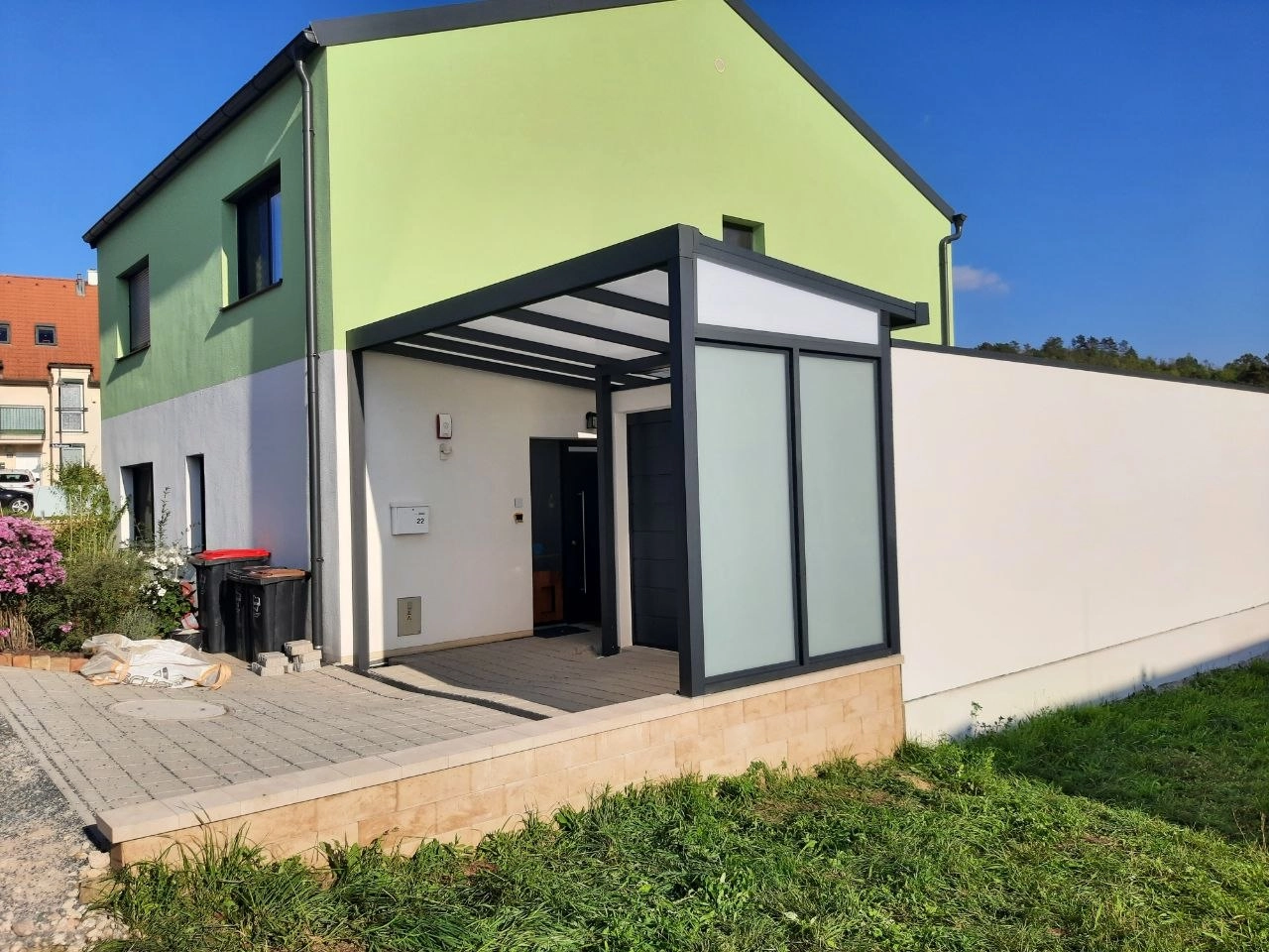 Kompakte Aluminium-Überdachung mit seitlichem Element vor einer Garage am grünen Wohnhaus